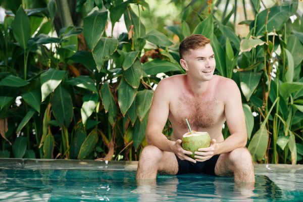 Smiling handsome young man resting in swimming pool on hot day and drinking tasty refreshing coconut cocktail Frostproof FL