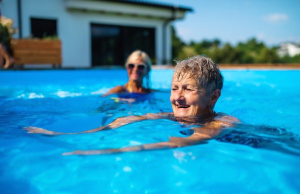 Portrait of senior woman with friends in swimming pool outdoors in backyard in Davenport, FL